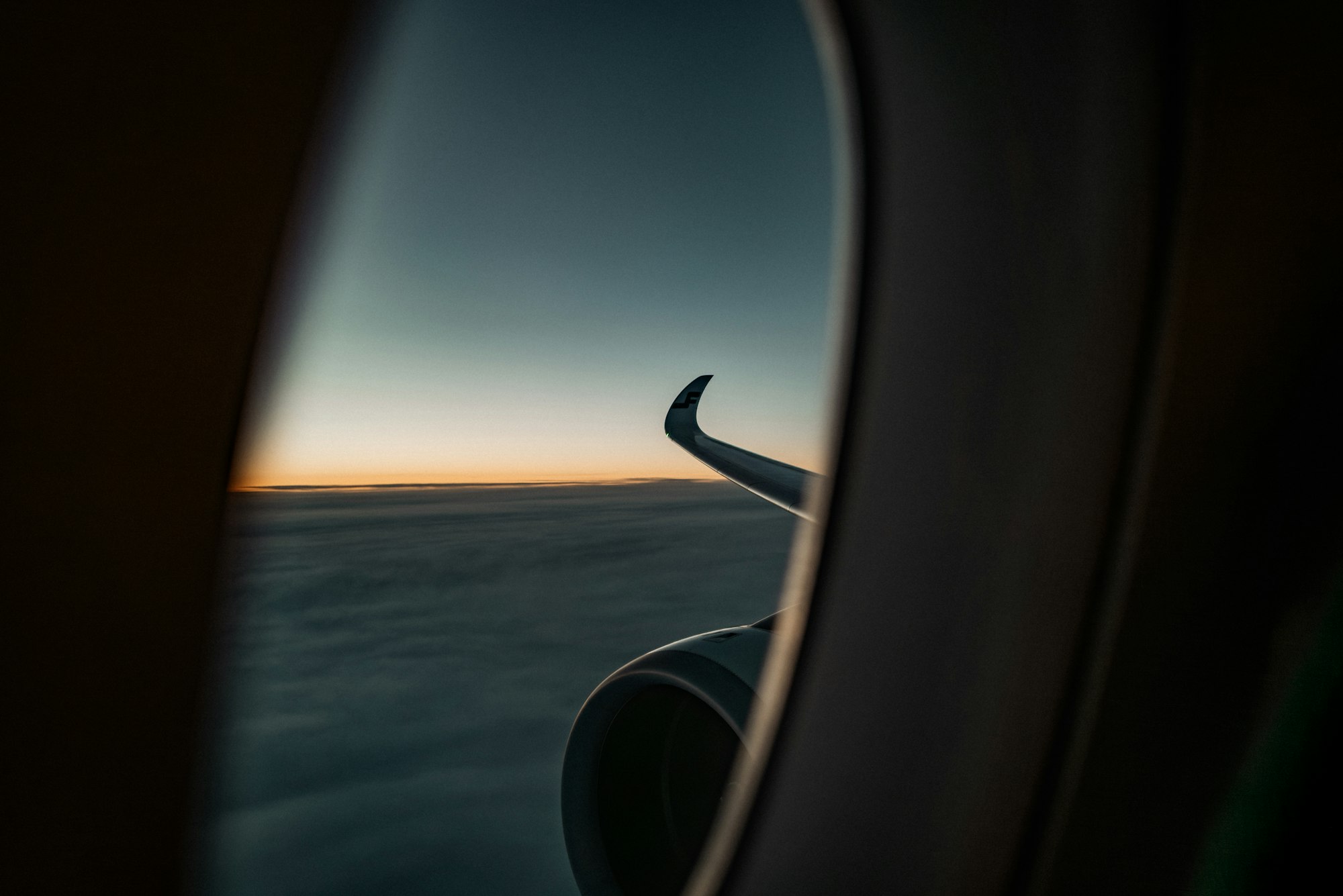 An airplane wing above a layer of clouds, lit by a low sun near the horizon.